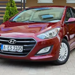 Czerwony Hyundai i30 1.6 CRDi lśni w słońcu, zaparkowany na kostce brukowej przed domem.