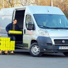Mężczyzna rozładowuje żółte paczki z Fiata Ducato 2.3 Multijet.
