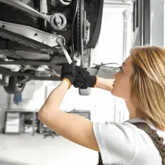 Mechanik pracuje pod samochodem, dokręcając śrubę wahacza. Sprawdź wymiana wahacza cena.