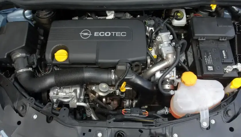 Silnik Opel Corsa D 1.2 benzyna. Widoczny jest czarny dekiel z napisem Ecotec, akumulator Varta oraz zbiornik płynu chłodniczego.