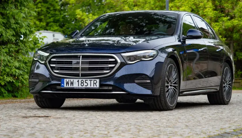 Elegancki, ciemnogranatowy Mercedes z napędem 4matic, zaparkowany na brukowanej nawierzchni, otoczony zielenią.