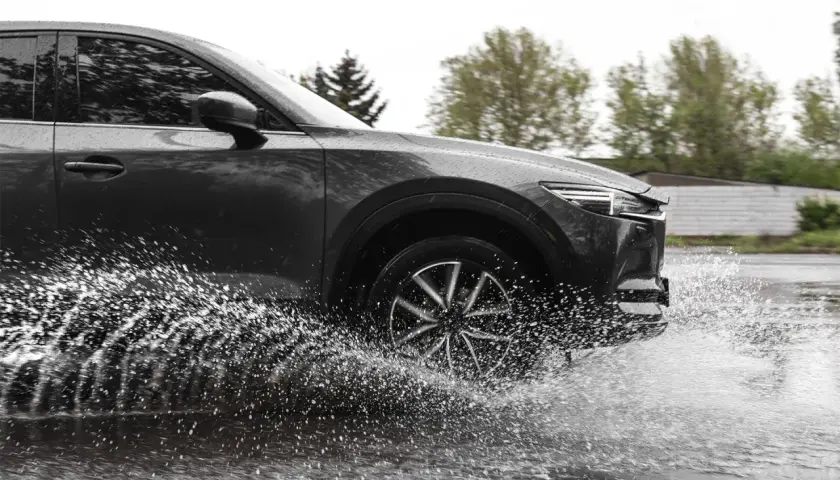 Ciemny samochód na mokrej drodze, koło rozpryskuje wodę, groźny aquaplaning.