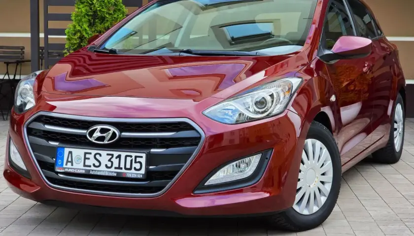 Czerwony Hyundai i30 1.6 CRDi lśni w słońcu, zaparkowany na kostce brukowej przed domem.