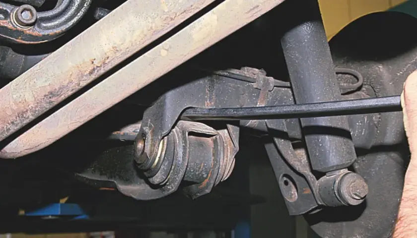 Mechanik pracuje przy wahaczu w samochodzie, używając narzędzia do regulacji.