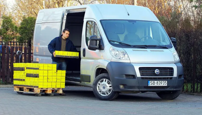 Mężczyzna rozładowuje żółte paczki z Fiata Ducato 2.3 Multijet.