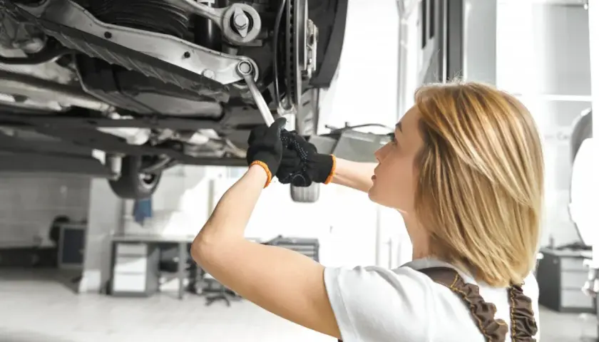 Mechanik pracuje pod samochodem, dokręcając śrubę wahacza. Sprawdź wymiana wahacza cena.