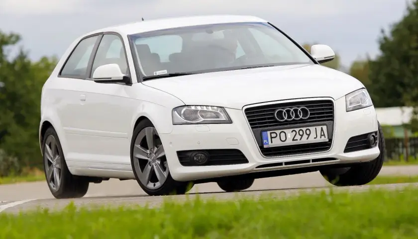 Białe Audi A3 8P 2.0 TDI na zakręcie, z zieloną trawą na pierwszym planie.