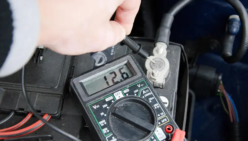 Pomiar napięcia akumulatora multimetrem. 12.6V to prawidłowy odczyt, ale niskie napięcie może być jednym z objawów alternatora.