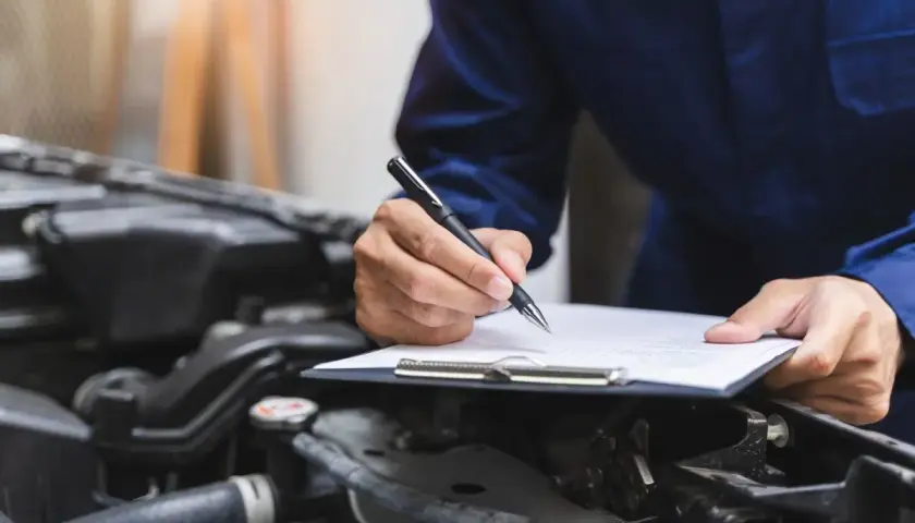 Mechanik spisuje protokół przeglądu samochodu po terminie, notując stan techniczny pojazdu.