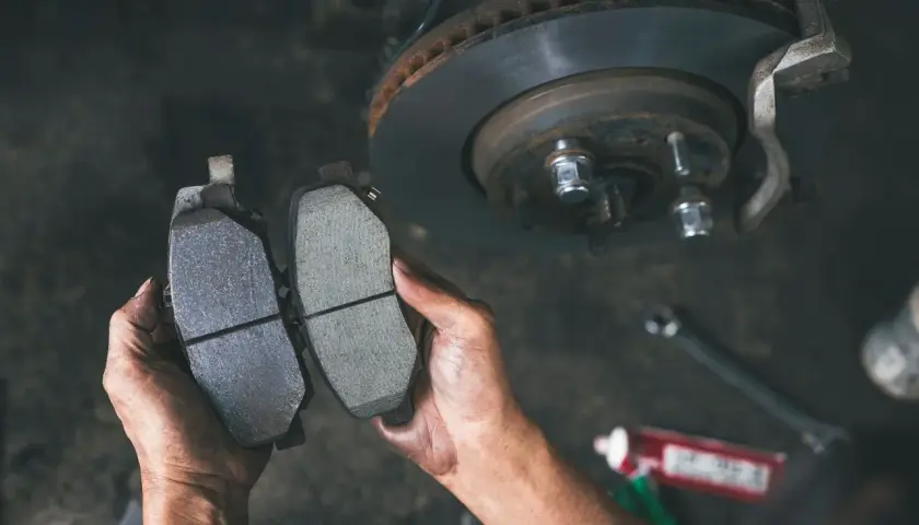 Ręce mechanika porównują zużyte i nowe klocki hamulcowe. Czas na wymianę klocków hamulcowych w samochodzie.