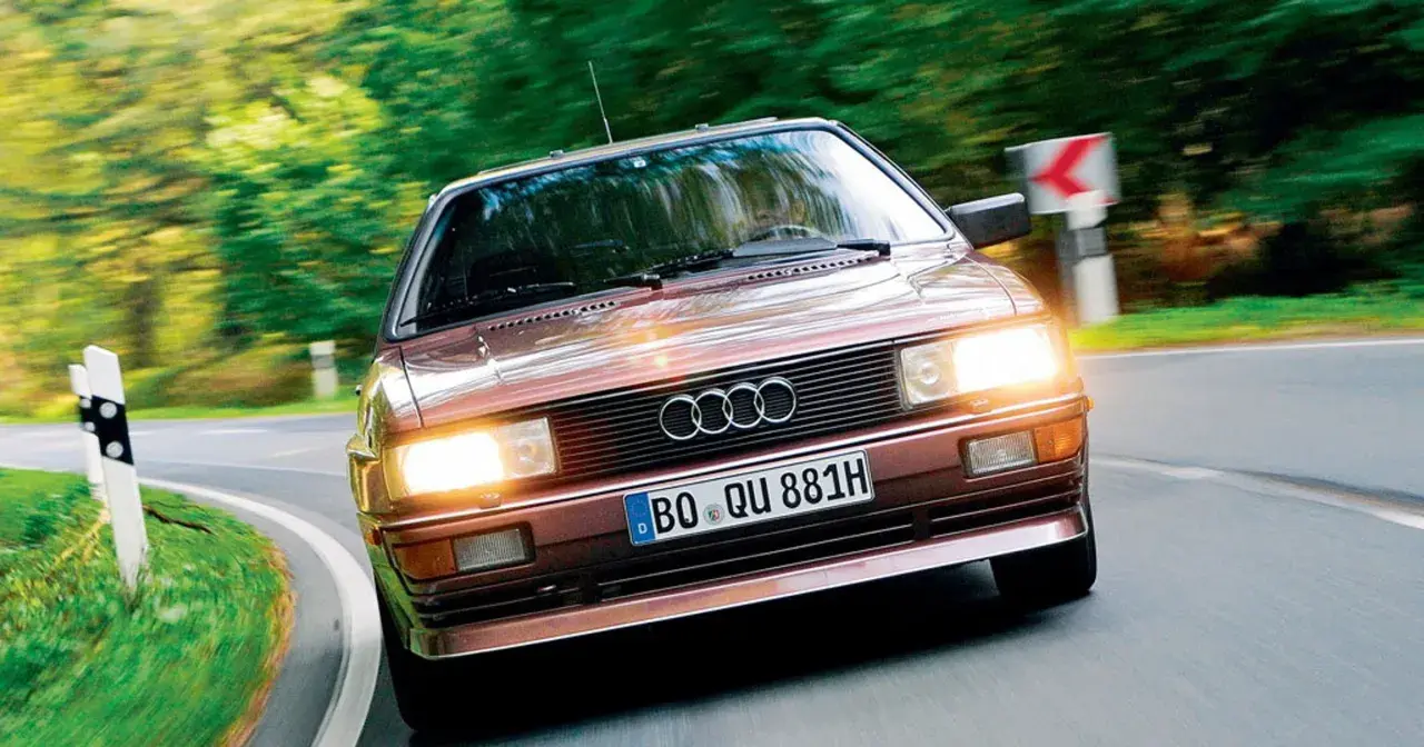 Klasyczny, brązowy Audi quattro z lat 80. pędzi po krętej, leśnej drodze.
