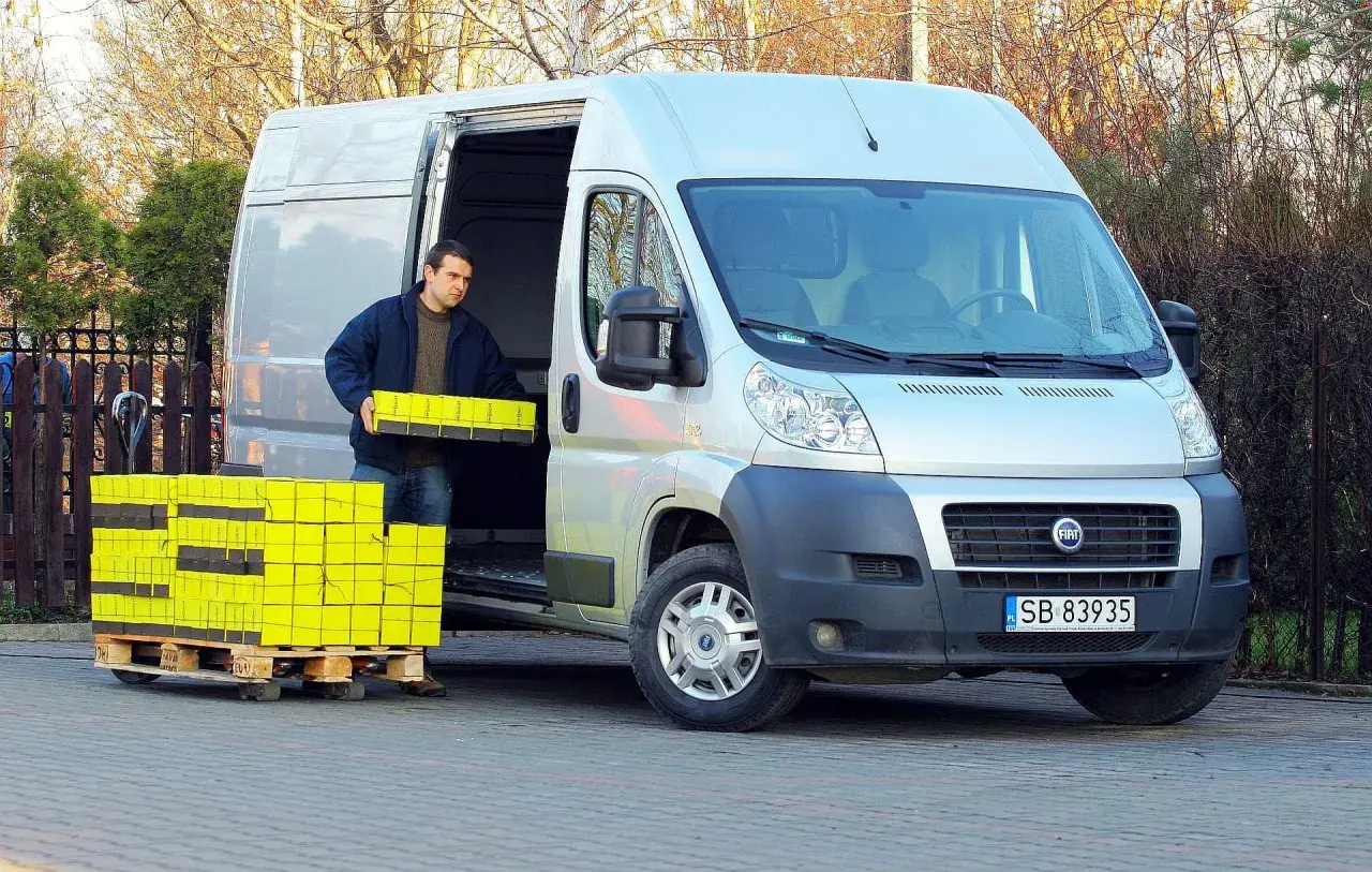 Mężczyzna rozładowuje żółte paczki z Fiata Ducato 2.3 Multijet.