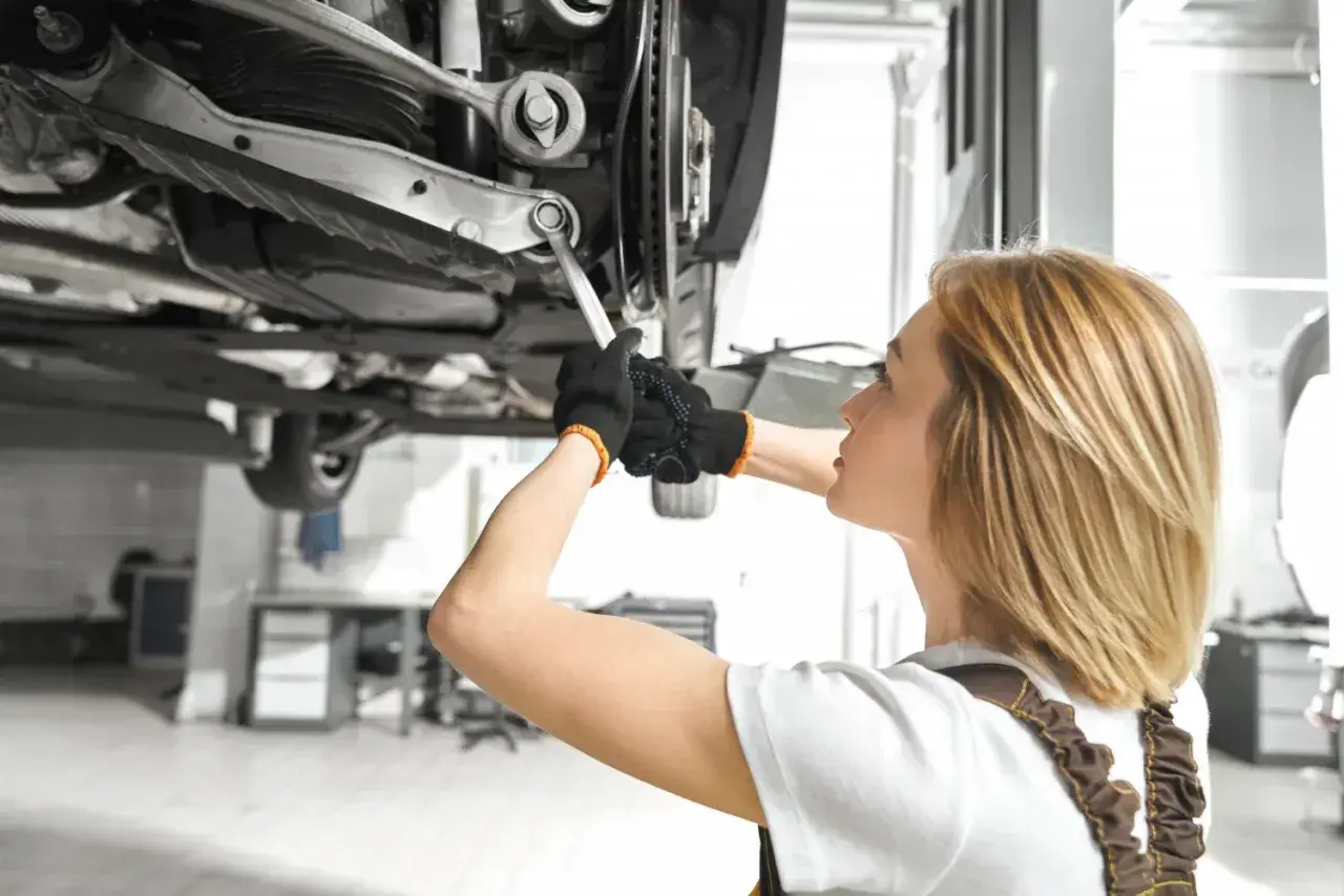 Mechanik pracuje pod samochodem, dokręcając śrubę wahacza. Sprawdź wymiana wahacza cena.