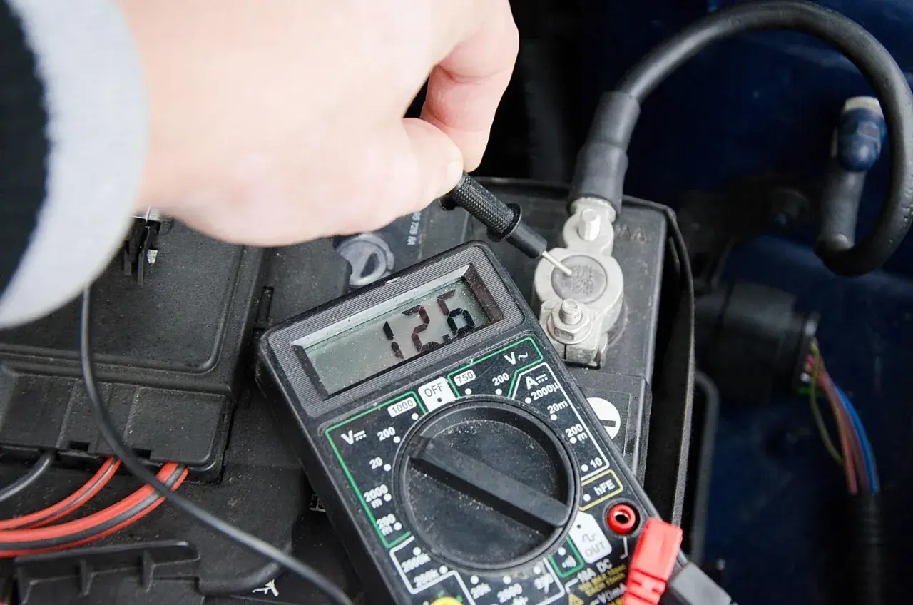 Pomiar napięcia akumulatora multimetrem. 12.6V to prawidłowy odczyt, ale niskie napięcie może być jednym z objawów alternatora.