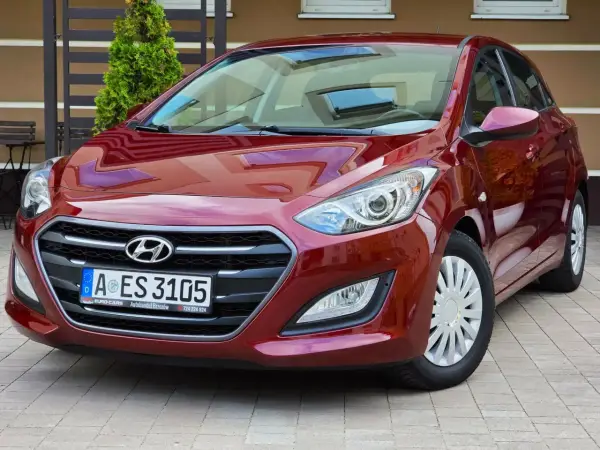 Czerwony Hyundai i30 1.6 CRDi lśni w słońcu, zaparkowany na kostce brukowej przed domem.